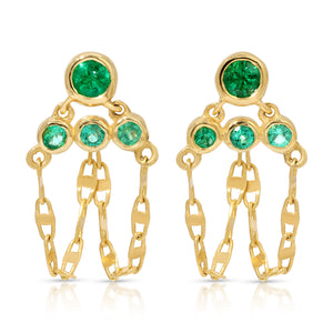 A pair of handcrafted 14k yellow gold post drop earrings featuring four round bezel-set green emerald gemstones on each earring arranged in a tiered, triangular cluster. Three delicate loops of mariner link chain suspend gracefully beneath the stones, creating a fluid dangle fringe against a clean white background. A pair of handcrafted 14k yellow gold post drop earrings featuring four round bezel-set green emerald gemstones on each earring arranged in a tiered, triangular cluster. Three delicate loops of mariner link chain suspend gracefully beneath the stones, creating a fluid dangle fringe against a clean white background.