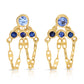 A pair of handcrafted 14k yellow gold Anna drop earrings featuring a tiered geometric setting with light blue and dark blue natural sapphires, suspended above delicate looping strands of mariner link chain against a plain white background.